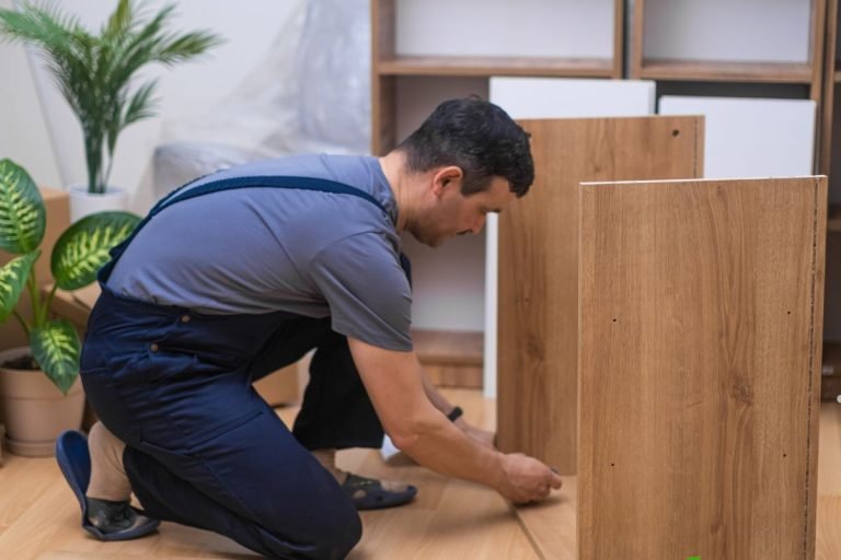 A person in dark overalls is assembling wooden furniture, focusing on connecting two pieces in a well-lit, modern room.